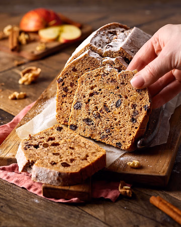 Saftiges Apfelbrot mit Nüssen, aufgeschnitten auf einem Holzbrett.