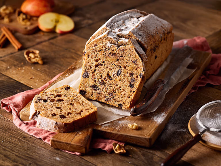 Saftiges Apfelbrot mit Nüssen, aufgeschnitten auf einem Holzbrett.