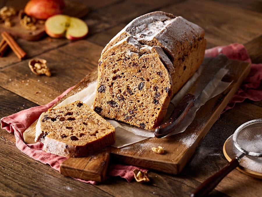 Saftiges Apfelbrot mit Nüssen, aufgeschnitten auf einem Holzbrett.