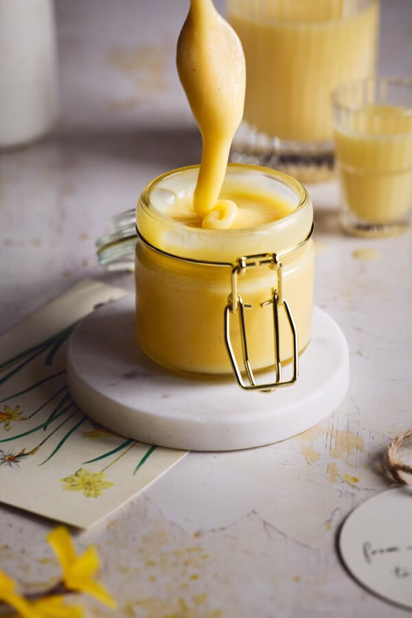 Ein Löffel mit zarter Schokoladencreme aus weißer Schokolade und Eierlikör wird aus einem Glas gehoben, die Creme zieht Fäden.