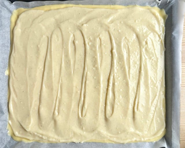 Vanillepudding-Schicht auf dem Rührteig verteilt für Apfelkuchen mit Streusel.
