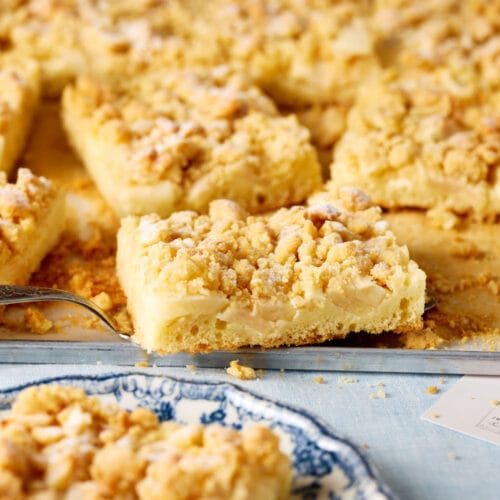 Saftiger Apfelkuchen mit Pudding und Streuseln, serviert auf einem hellen Kuchenteller – klassische Blechkuchen-Optik.