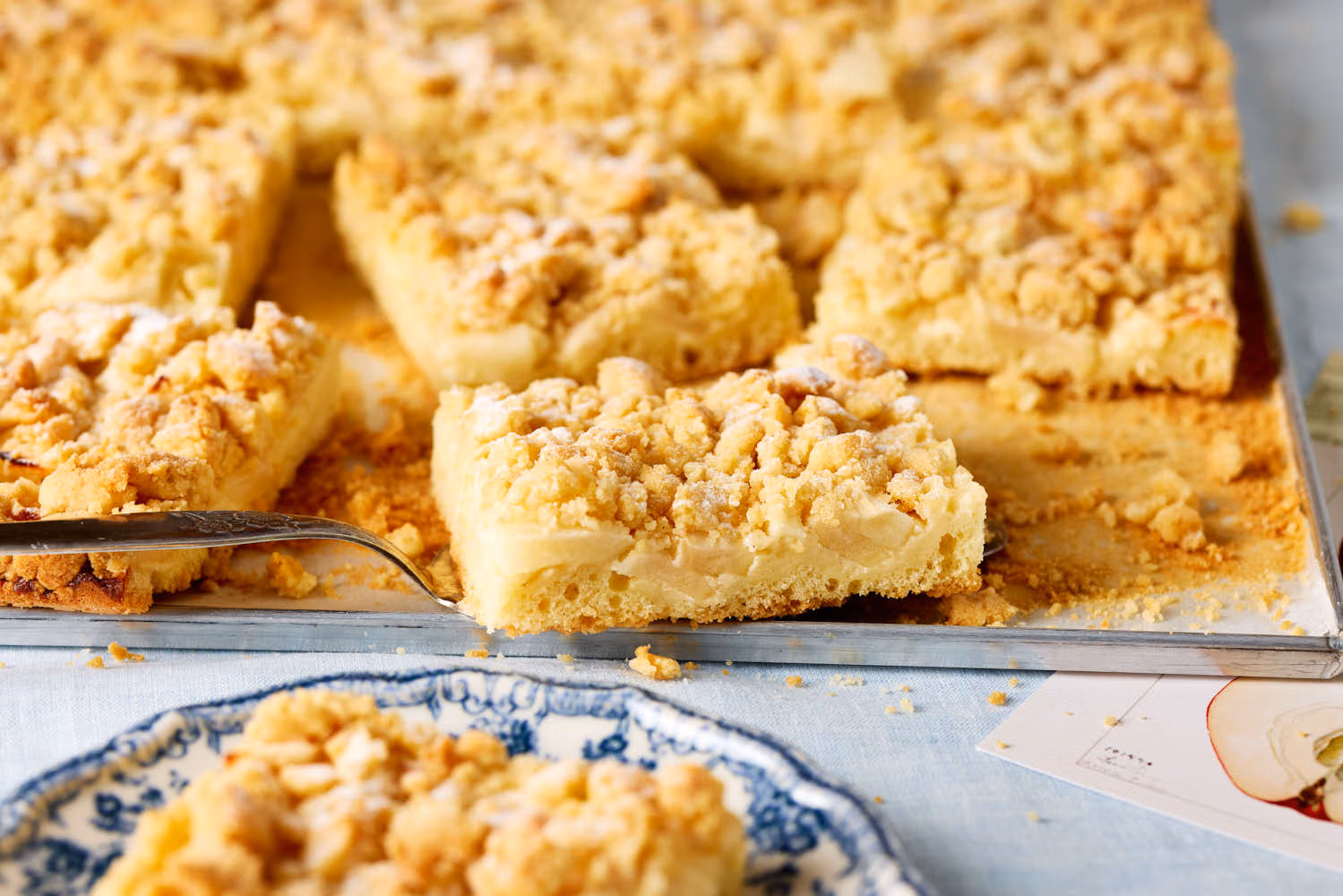 Saftiger Apfelkuchen mit Pudding und Streuseln, serviert auf einem hellen Kuchenteller – klassische Blechkuchen-Optik.