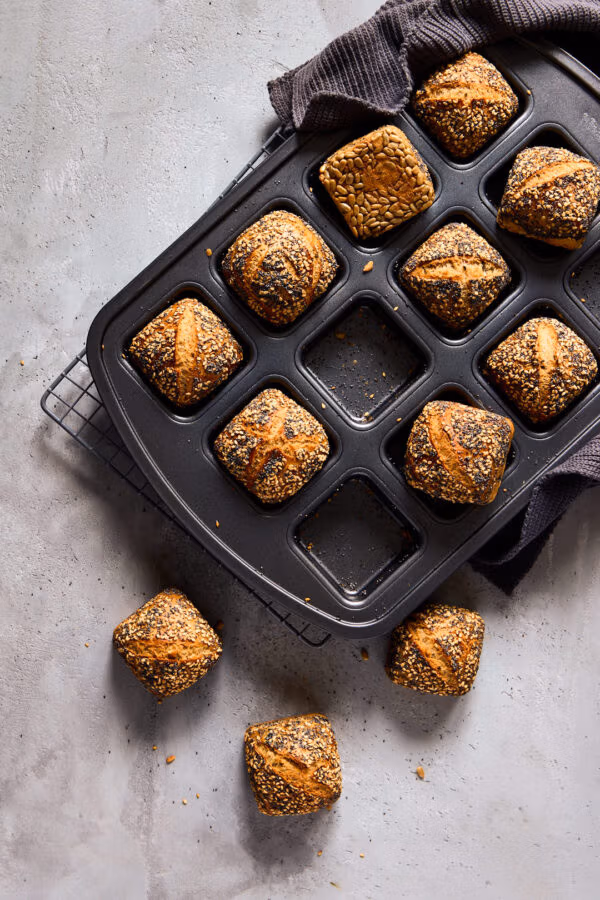 Mini-Weltmeisterbrötchen mit knuspriger Saatenkruste in einer Brownie-Form. Ein dunkles Küchentuch liegt an der Seite.