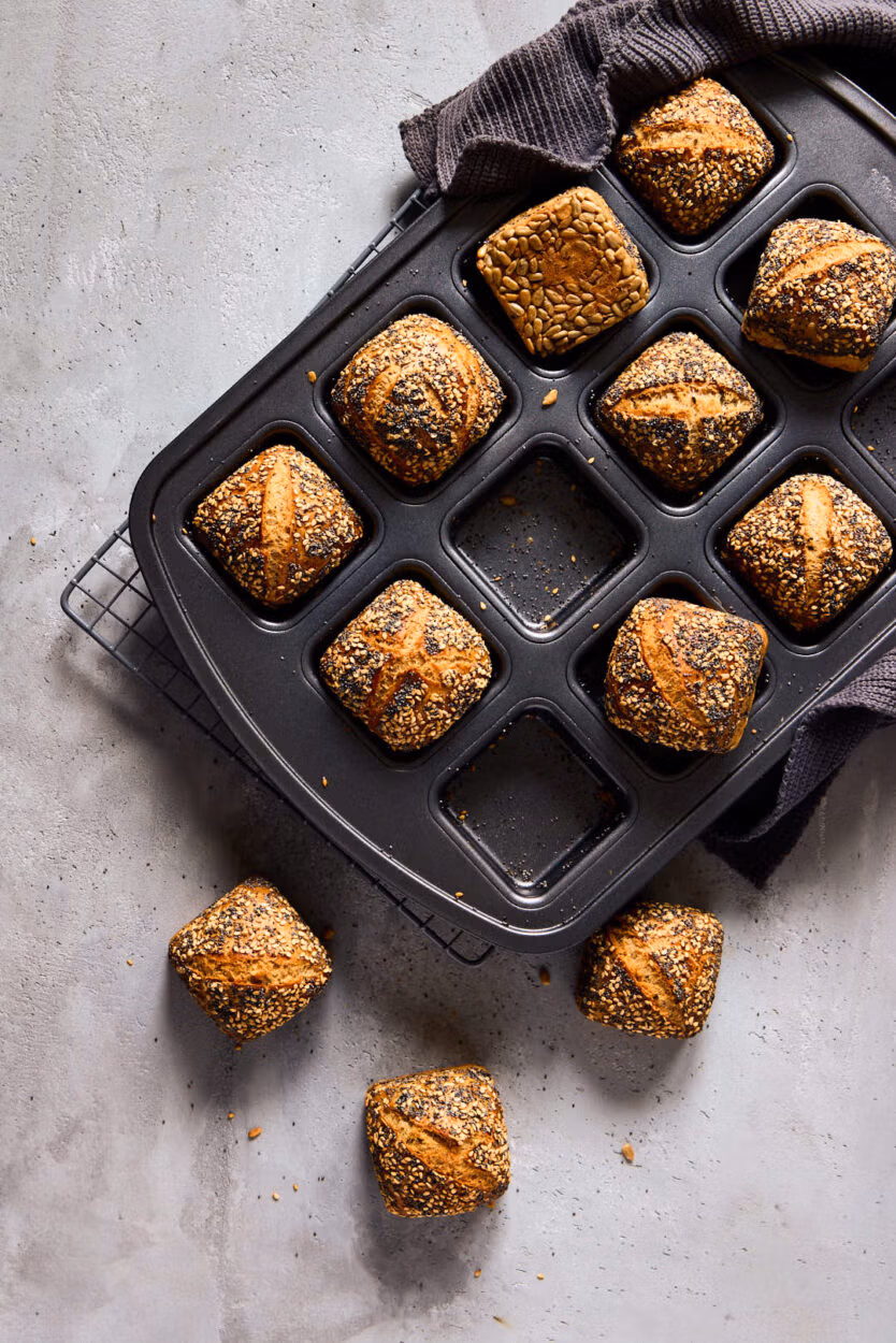 Mini-Weltmeisterbrötchen mit knuspriger Saatenkruste in einer Brownie-Form. Ein dunkles Küchentuch liegt an der Seite.