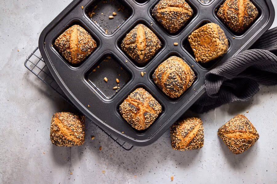 Mini-Weltmeisterbrötchen mit knuspriger Saatenkruste in einer Brownie-Form. Ein dunkles Küchentuch liegt an der Seite.