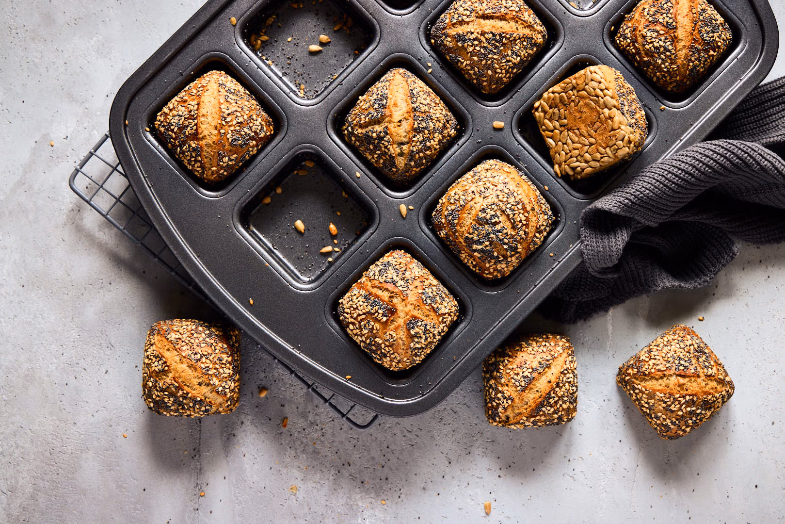Mini-Weltmeisterbrötchen mit knuspriger Saatenkruste in einer Brownie-Form. Ein dunkles Küchentuch liegt an der Seite.