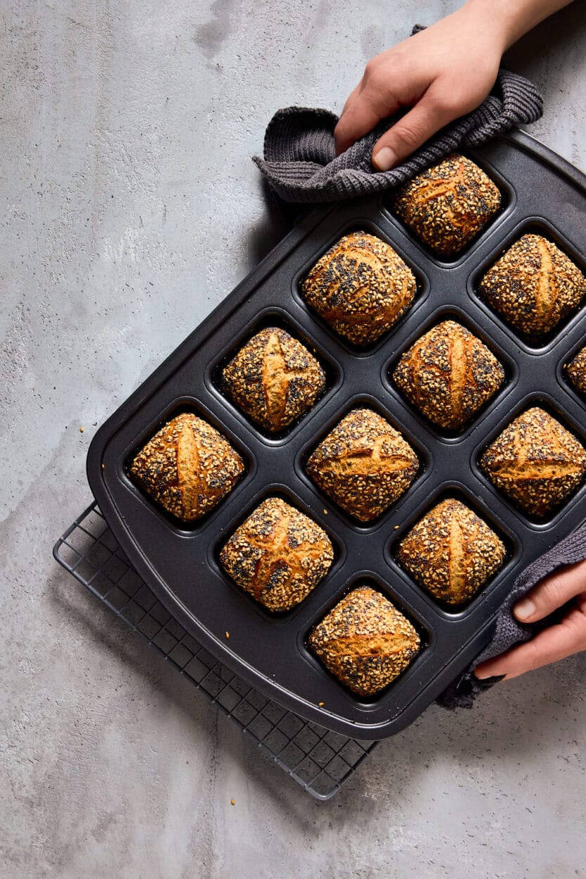 Zwei Hände heben eine Backform mit frisch gebackenen Mini-Weltmeisterbrötchen an.