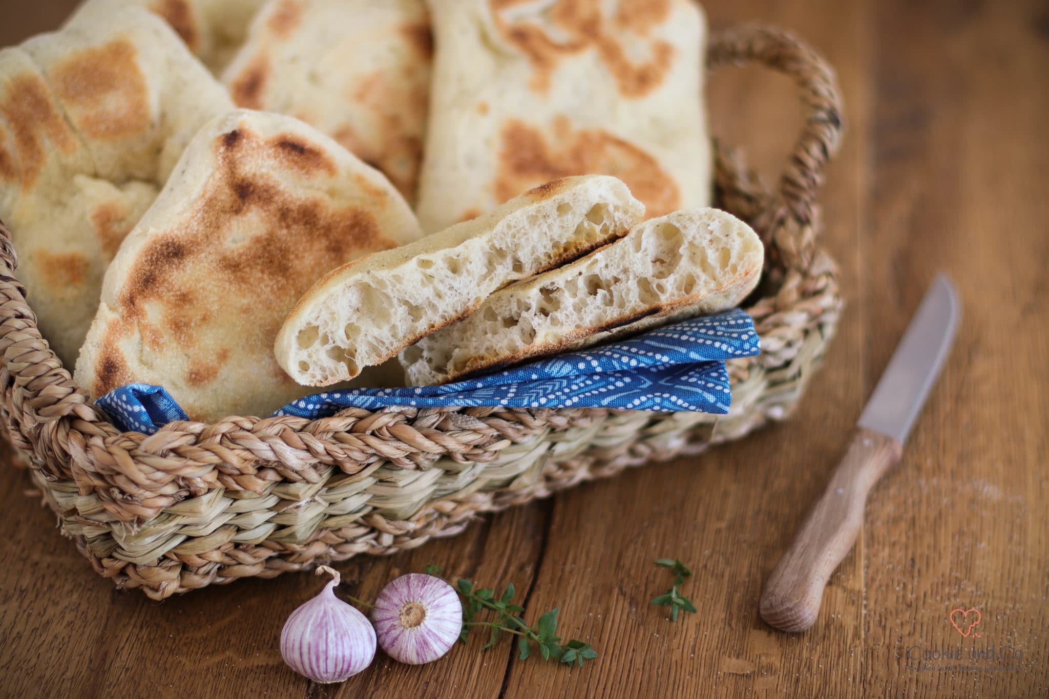 Grill- und Pfannenbrot in einem Brotkorb mit einem Messer und Knoblauch im Vordergrund.
