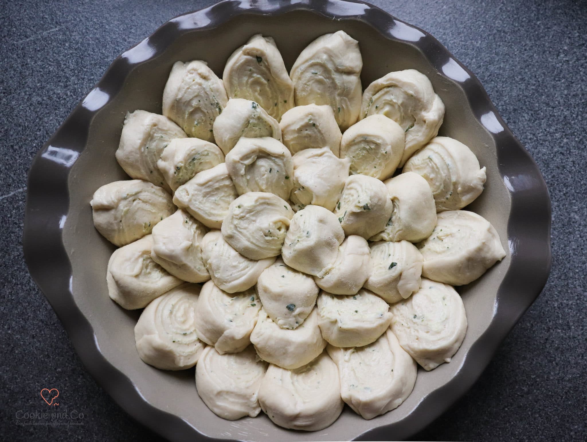 Fertig gefaltetes Zupfbrot mit Kräuterbutter in der Backform.