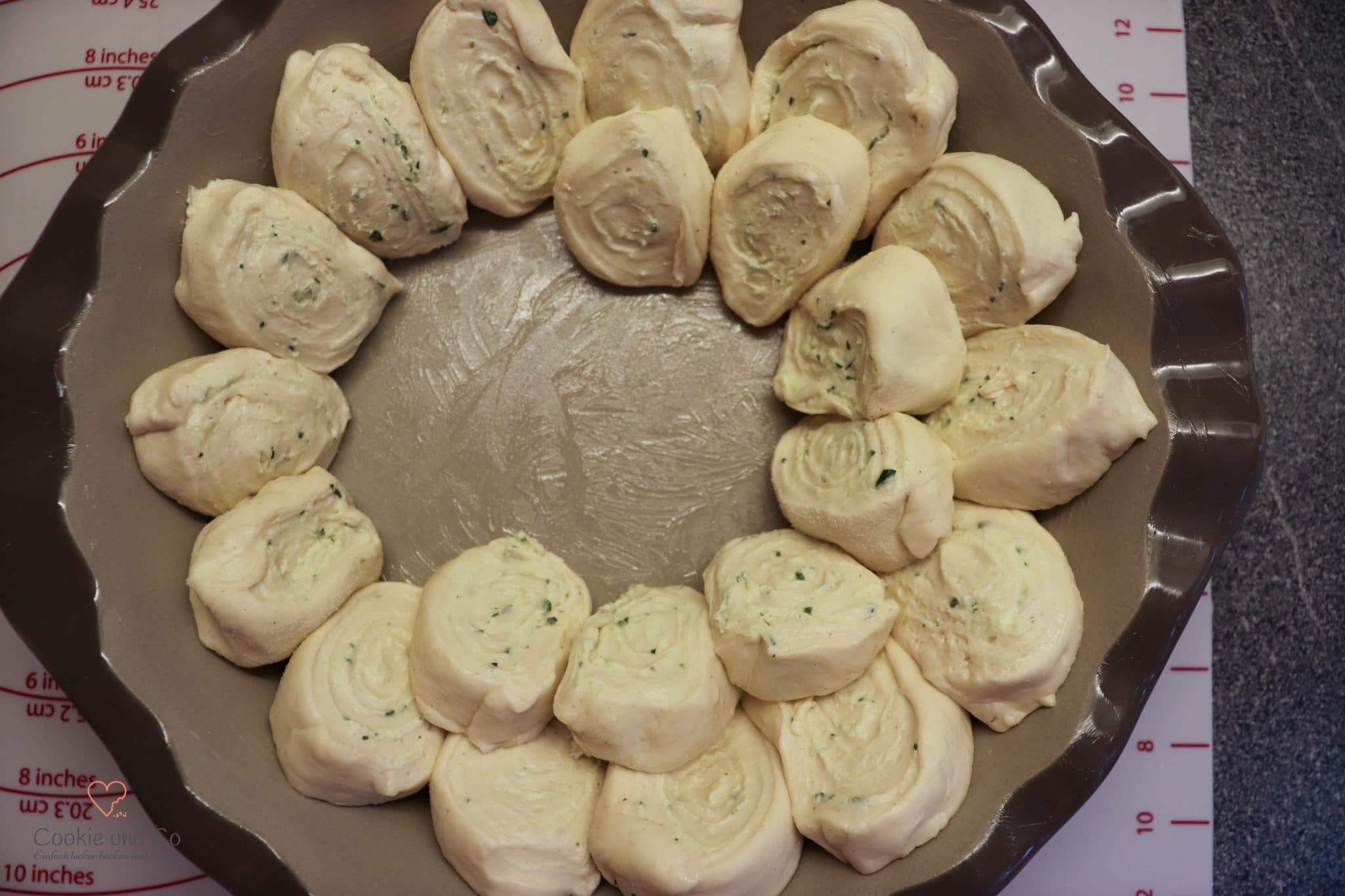 Geformten Hefeteig für Zupfbrot mit Kräuterbutter in die Backform schichten.