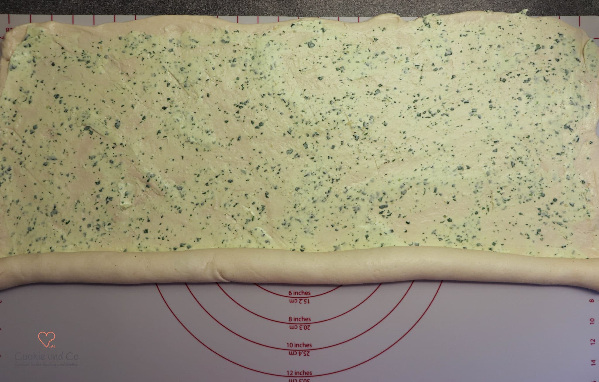 Mit Kräuterbutter gefüllten Hefeteig aufrollen für Zupfbrot.