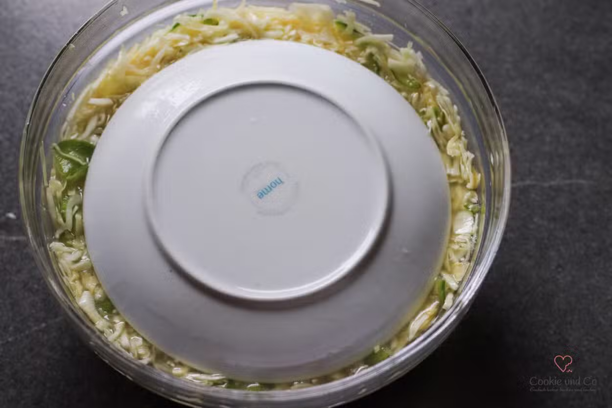 Weißkrautsalat in einer Glasschüssel mit einem Teller abgedeckt.