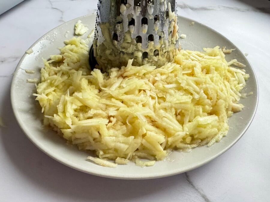 Geraspelte Äpfel mit einer Reibe auf einem Teller.