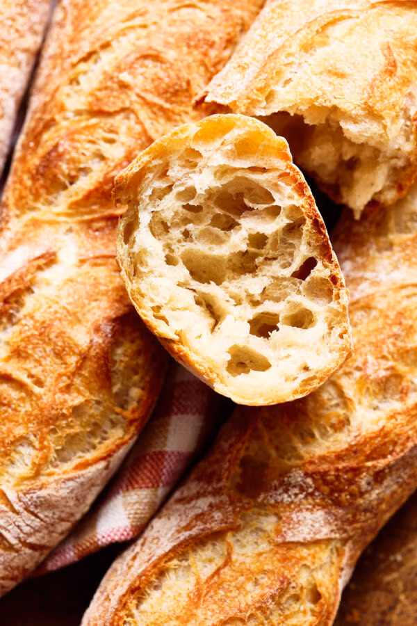 Französisches Baguette mit lockerer Krume, mit einem karierten Tuch auf einem französischen Holzbrett.