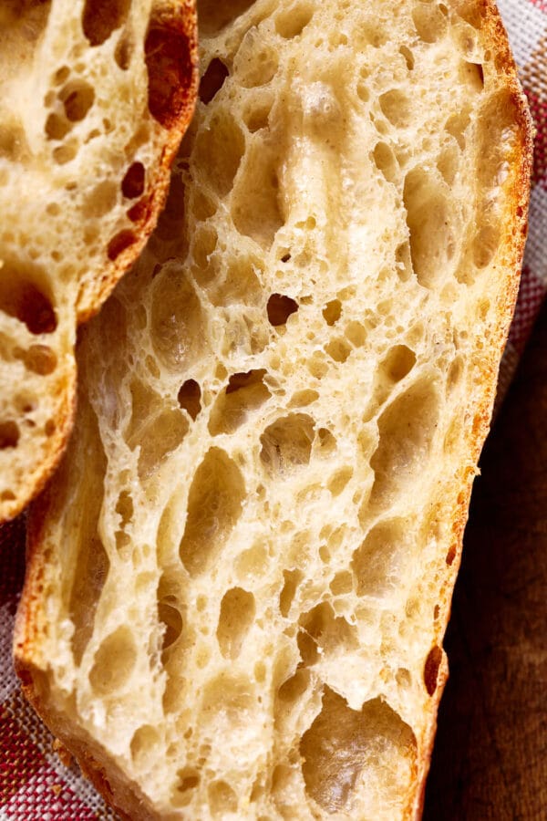 Nahaufnahme von einem französischen Baguette mit lockerer Krume, mit einem karierten Tuch auf einem rustikalen Holzbrett.