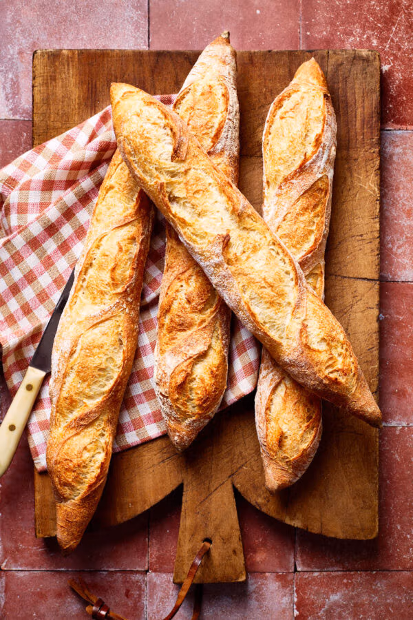 Französisches Baguette, mit einem karierten Tuch und Brotmesser auf einem französischen Holzbrett.