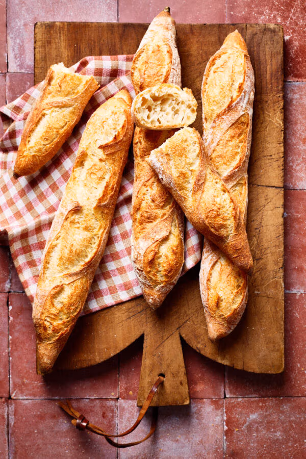 Französisches Baguette mit lockerer Krume, mit einem karierten Tuch und Brotmesser auf einem französischen Holzbrett.