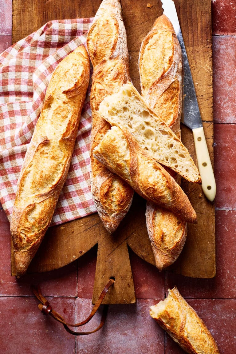Französisches Baguette mit lockerer Krume, mit einem karierten Tuch und Brotmesser auf einem französischen Holzbrett.