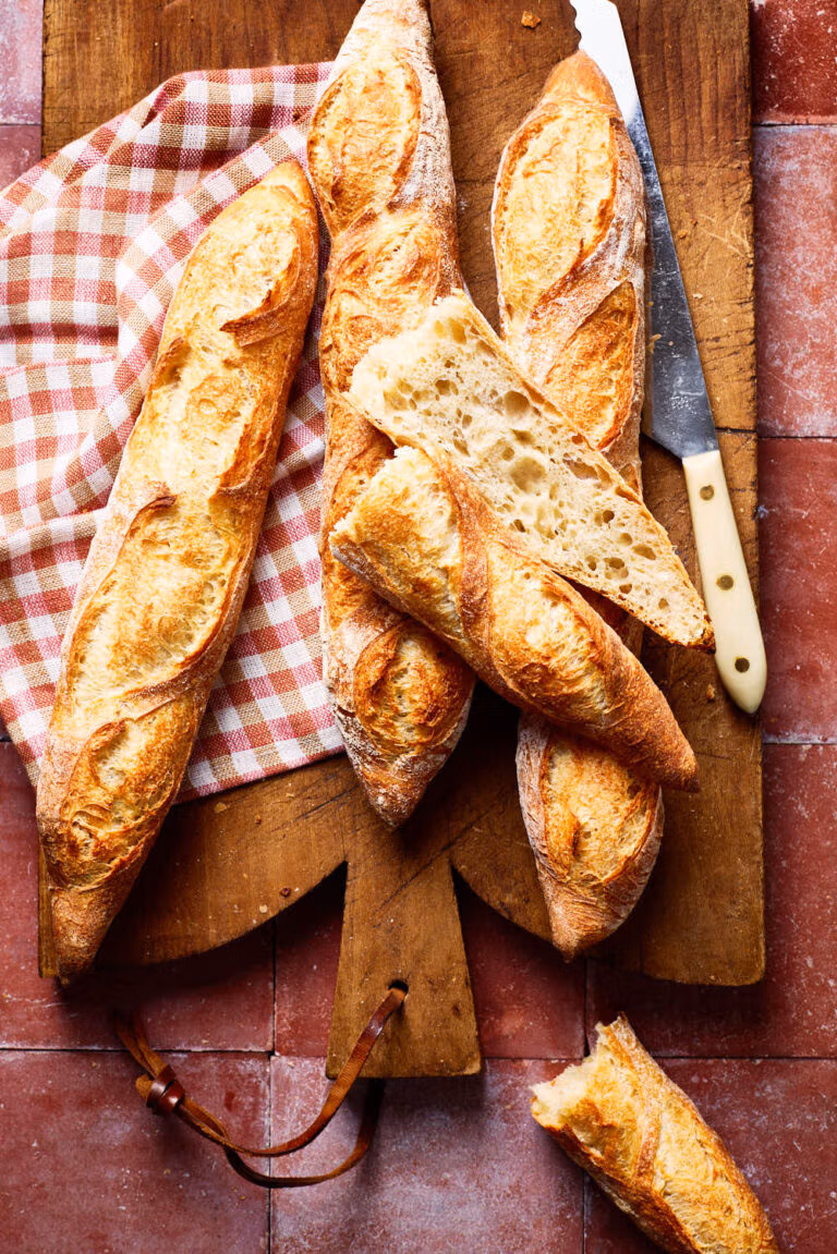 Französisches Baguette mit lockerer Krume, mit einem karierten Tuch und Brotmesser auf einem französischen Holzbrett.
