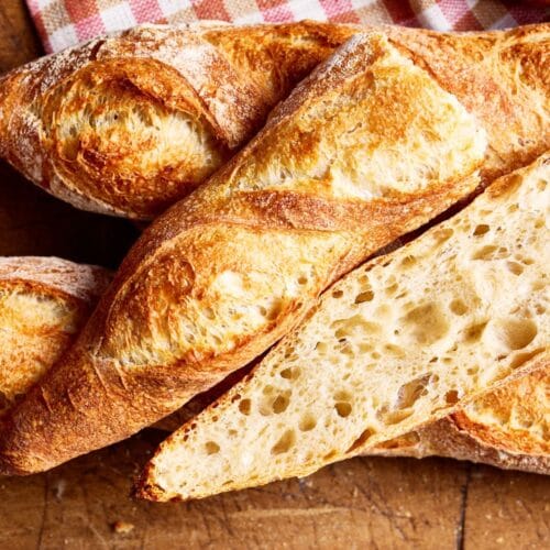 Französisches Baguette mit lockerer Krume, mit einem karierten Tuch auf einem französischen Holzbrett.
