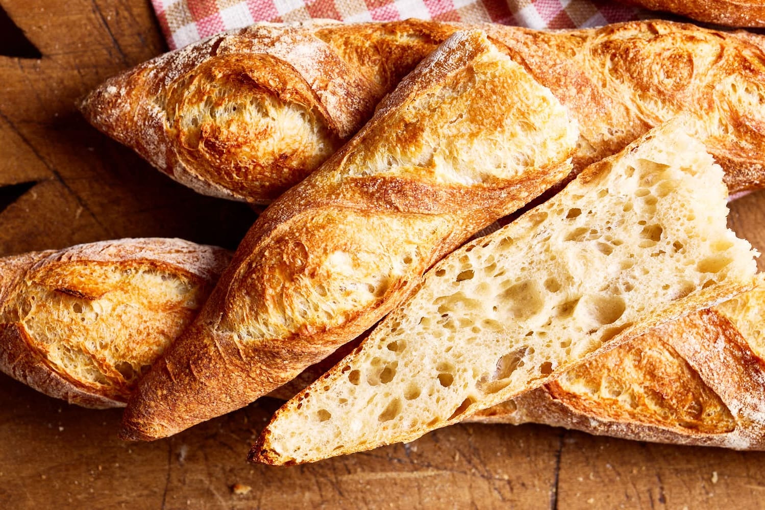 Französisches Baguette mit lockerer Krume, mit einem karierten Tuch auf einem französischen Holzbrett.
