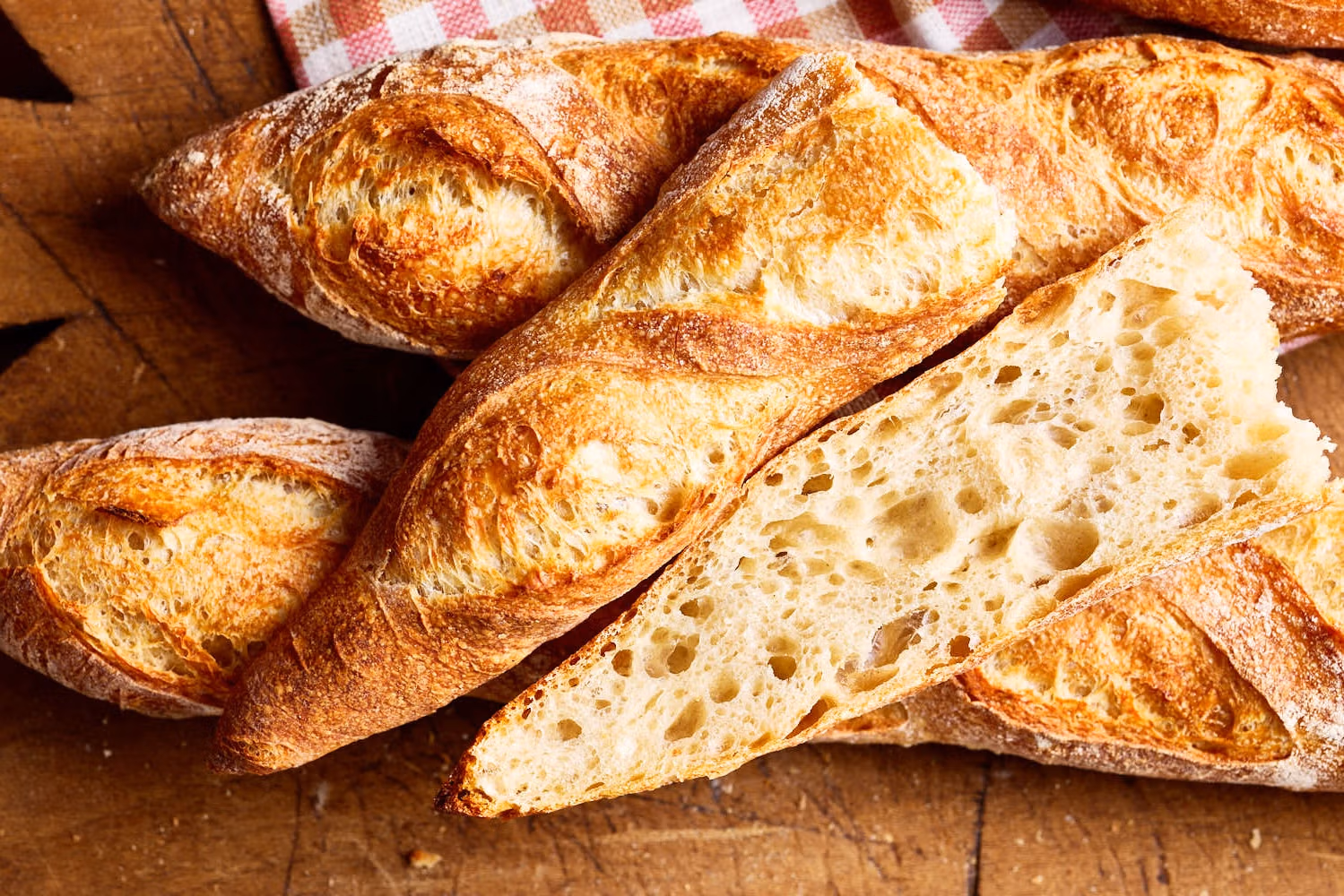 Französisches Baguette mit lockerer Krume, mit einem karierten Tuch auf einem französischen Holzbrett.