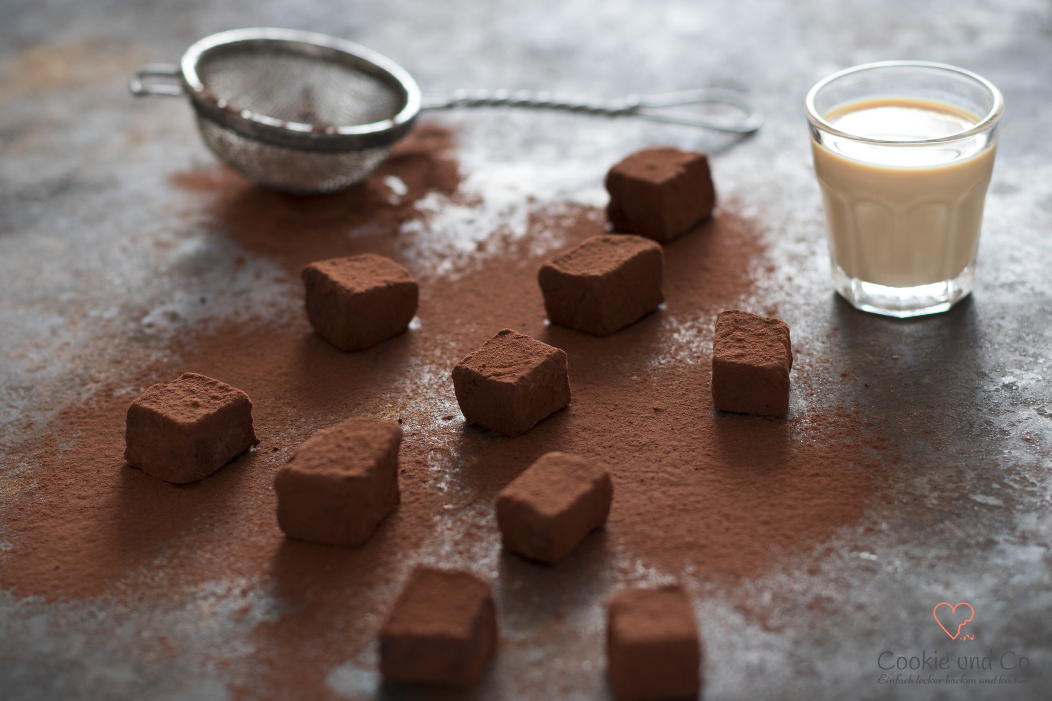 Baileys Trüffel, mit Kakao bestreut und einem Glas Baileys im Hintergrund.