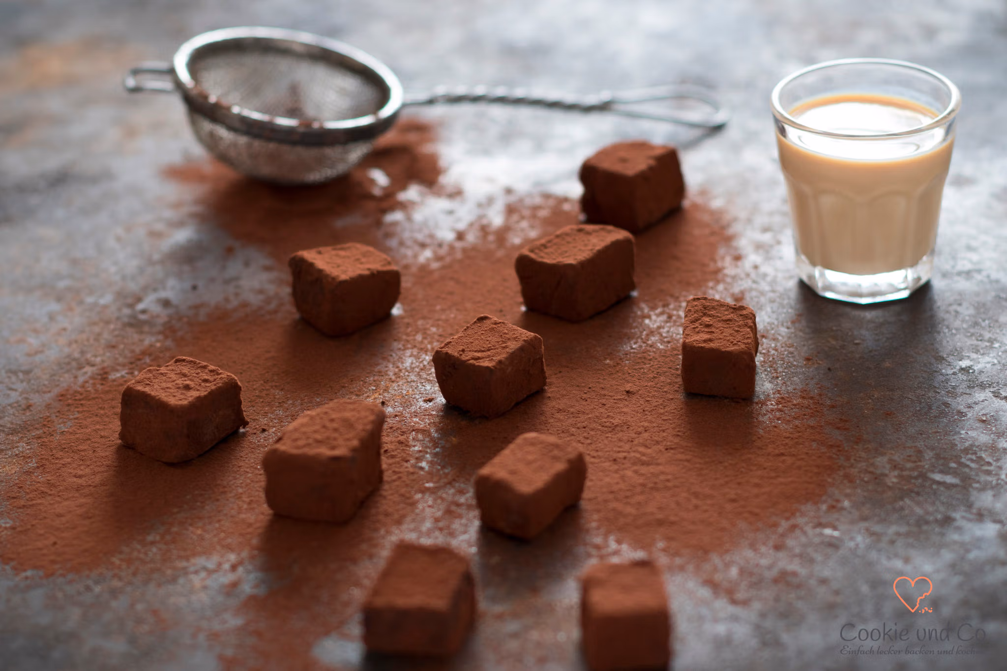 Baileys Trüffel, mit Kakao bestreut und einem Glas Baileys im Hintergrund.
