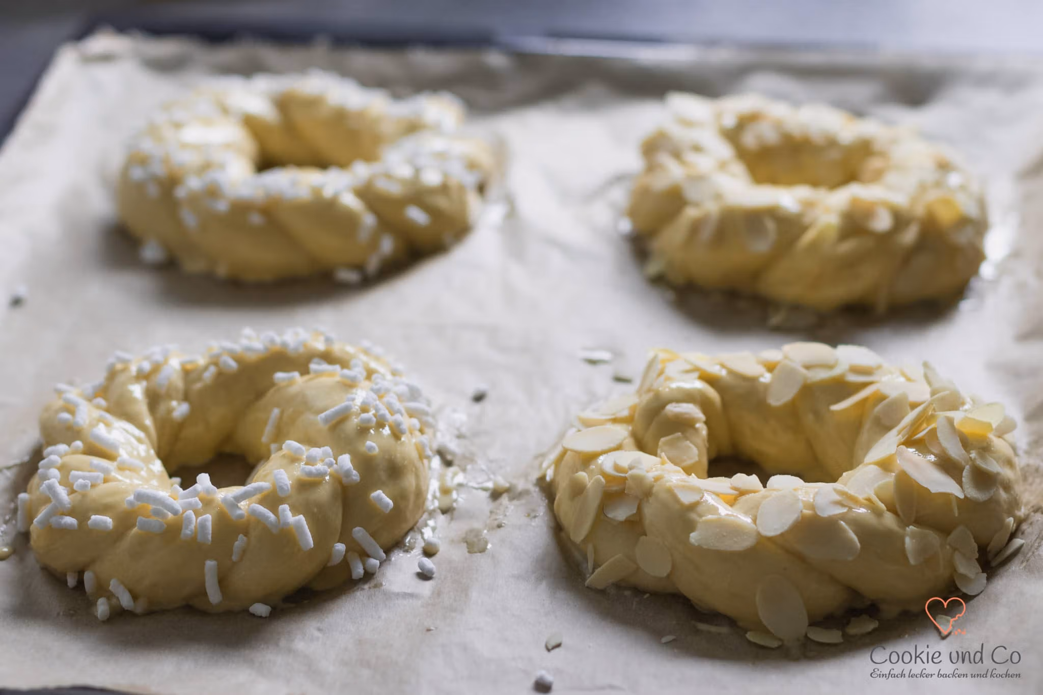 Geformter Hefeteig für Osterkränze auf einem Backblech mit Eistreiche und Mandeln sowie Hagelzucker bestreut.