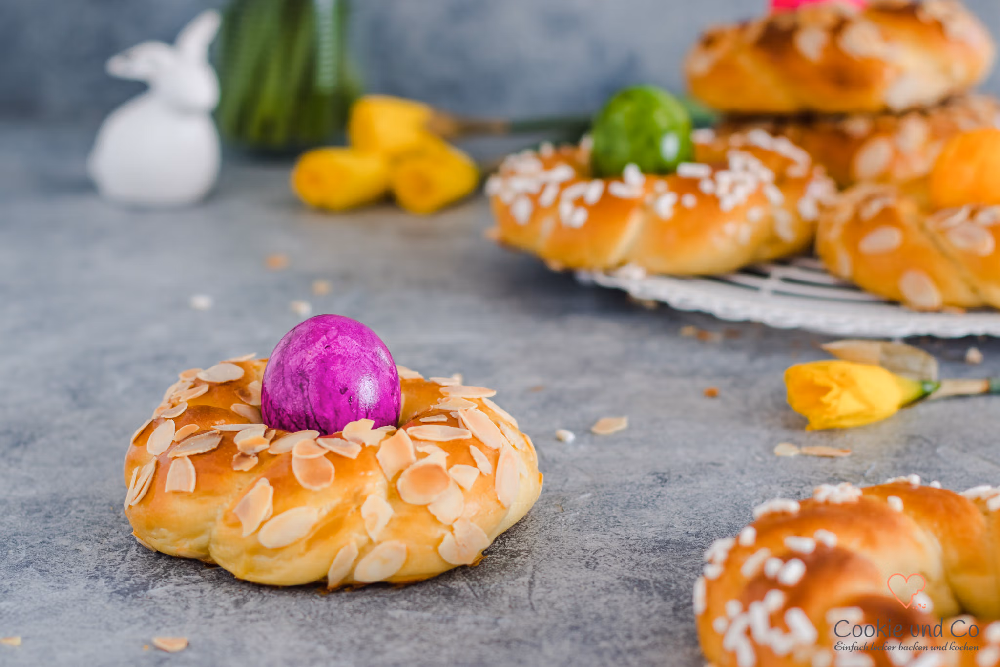 Dinkel-Osterkränze mit gefärbten Eiern und Narzissen im Hintergrund.