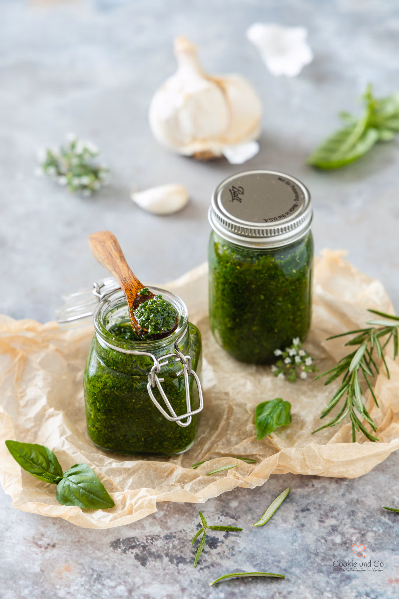 Mediterrane Kräuter-Gewürz-Paste in einem Glas mit frischen Kräutern und Knoblauch daneben.