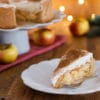 Kuchenstück von einer Apfel-Glögg-Torte (Apfel-Wein-Torte) auf einem Teller mit Weihnachtsbeleuchtung im Hintergrund.