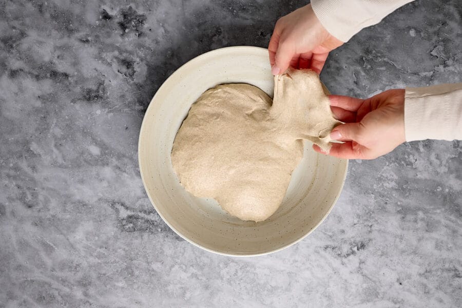 Fenstertest beim ausgegekneteten Teig für ein Mischbrot mit Sauerteig in einer großen Keramikschüssel.