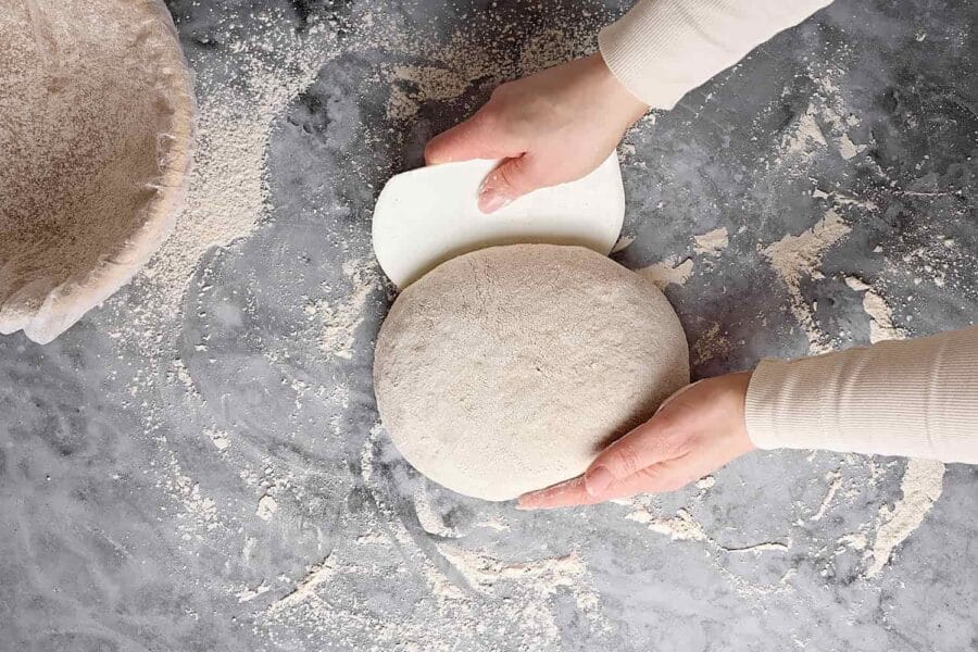 Teig für Mischbrot mit Sauerteig auf der bemehlten Arbeitsfläche rund formen.