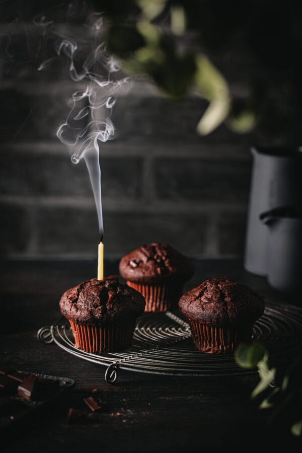Schokoladenmuffins mit einer ausgepusteten Kerze auf einem Kuchengitter.
