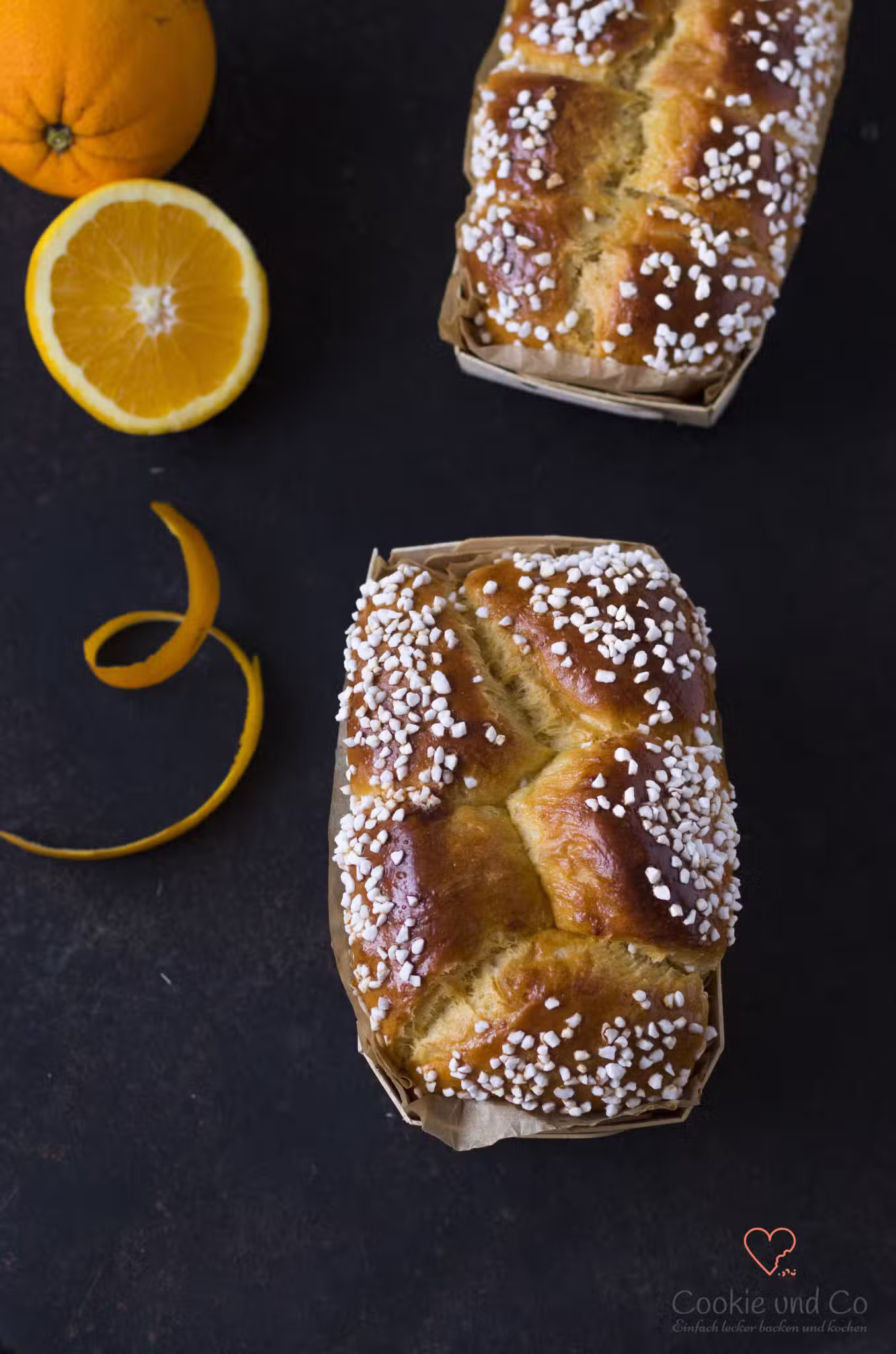 Dinkel-Brioche in einer Holzbackform, mit Hagelzucker bestreut und einer Orange daneben.