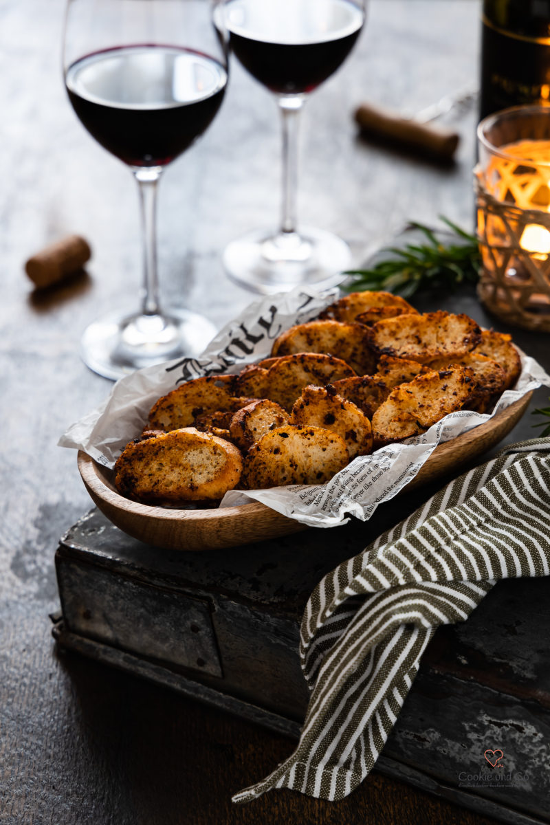 Selbstgemachte Chips aus altbackenem Brot in einer Holzschale mit Rotwein im Hintergrund