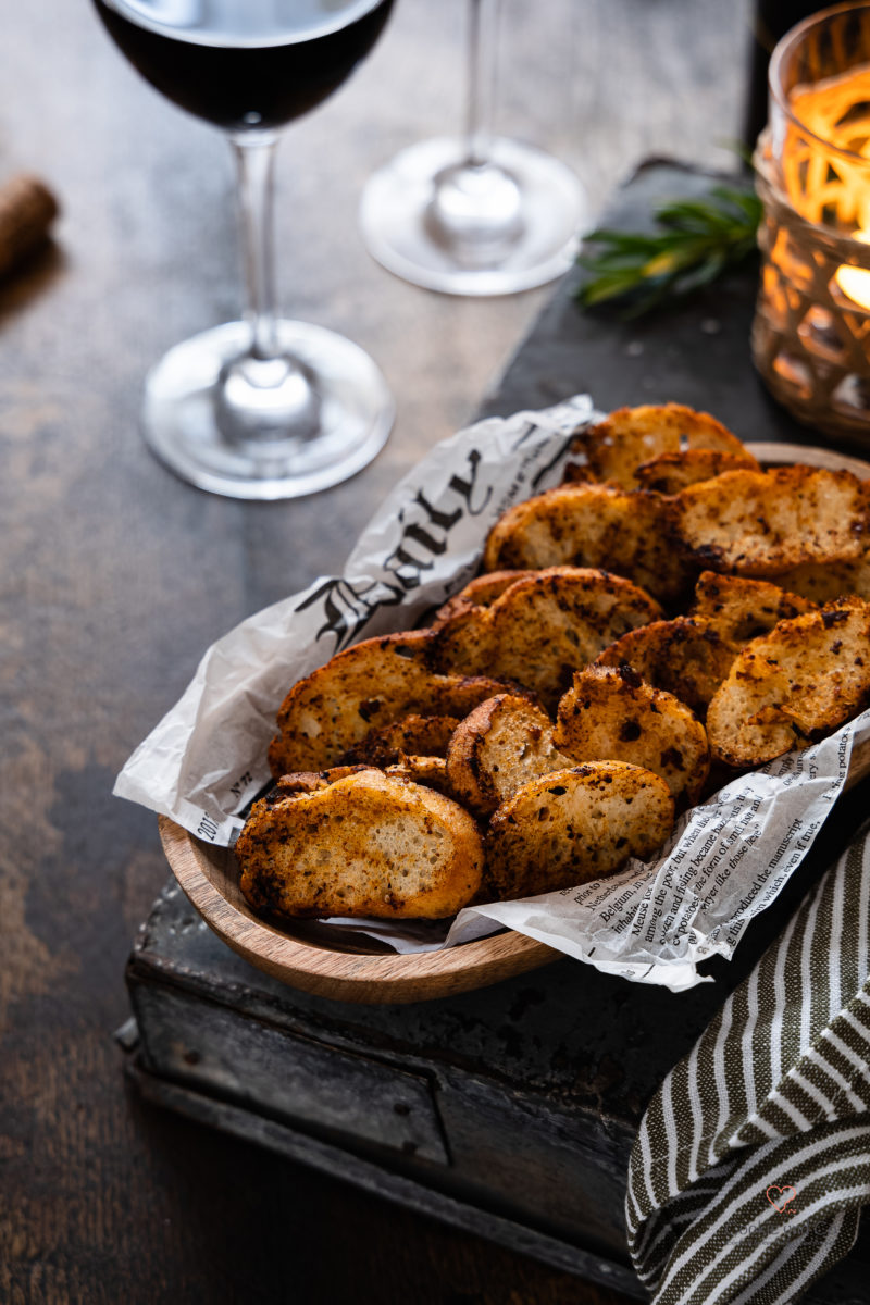 Selbstgemachte Brotchips in einer Holzschale mit Rotwein im Hintergrund