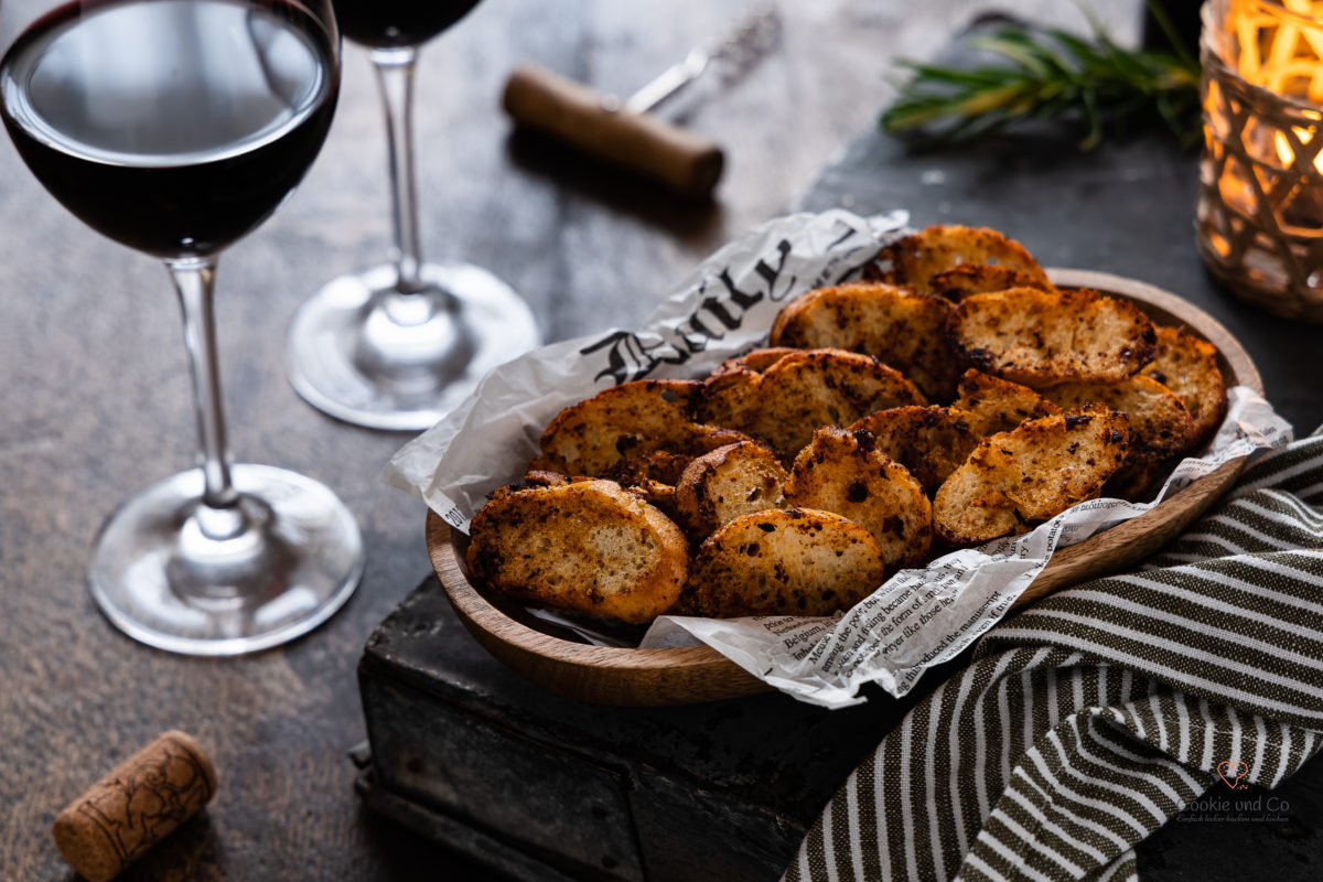 Selbstgemachte Brotchips in einer Holzschale mit Rotwein im Hintergrund