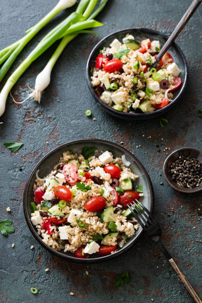 Reissalat nach griechischer Art in eier Schale mit einer Gabel und Lauchzwiebeln im Hintergrund.