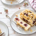 Ein Kirsch-Streuselkuchen auf einem Teller mit einer Gabel und Blumen im Hintergrund (schneller Blechkuchen aus Rührteig)