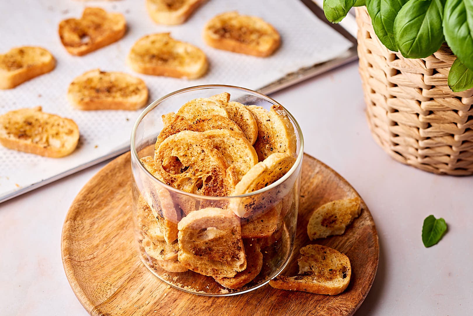 Selbstgemachte Brotchips in einem Glas mit einem Blech mit Brotchips im Hintergrund.