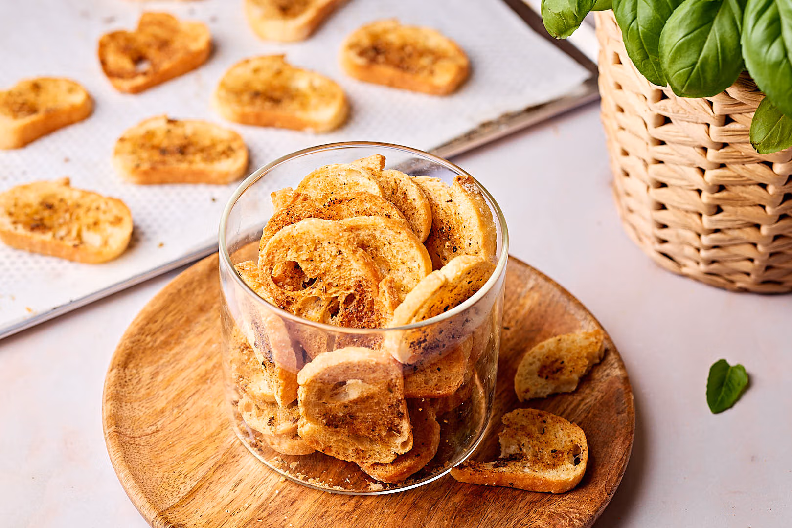 Selbstgemachte Brotchips in einem Glas mit einem Blech mit Brotchips im Hintergrund.
