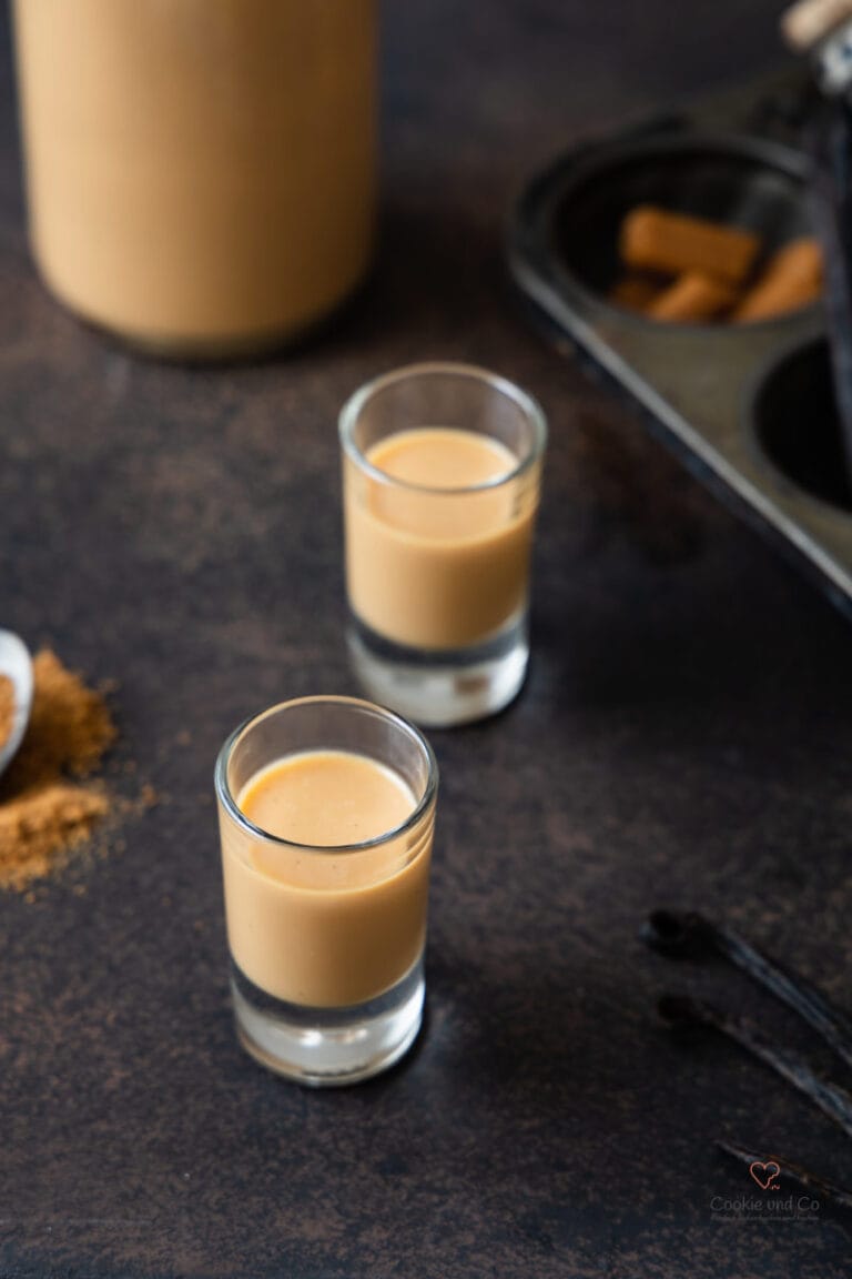 Selbst gemachtzer Karamell-Sahne-Likör in zwei Shotgläsern mit einer Likörflasche daneben.