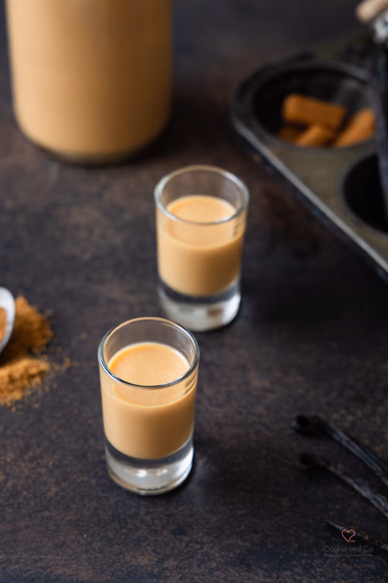 Selbst gemachtzer Karamell-Sahne-Likör in zwei Shotgläsern mit einer Likörflasche daneben.