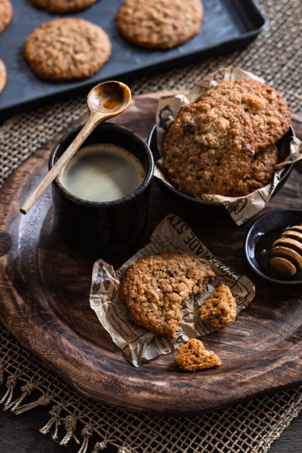 Gesündere Müslicookies auf einem Holzteller mit einer Tasse Kaffee im Hintergrund.