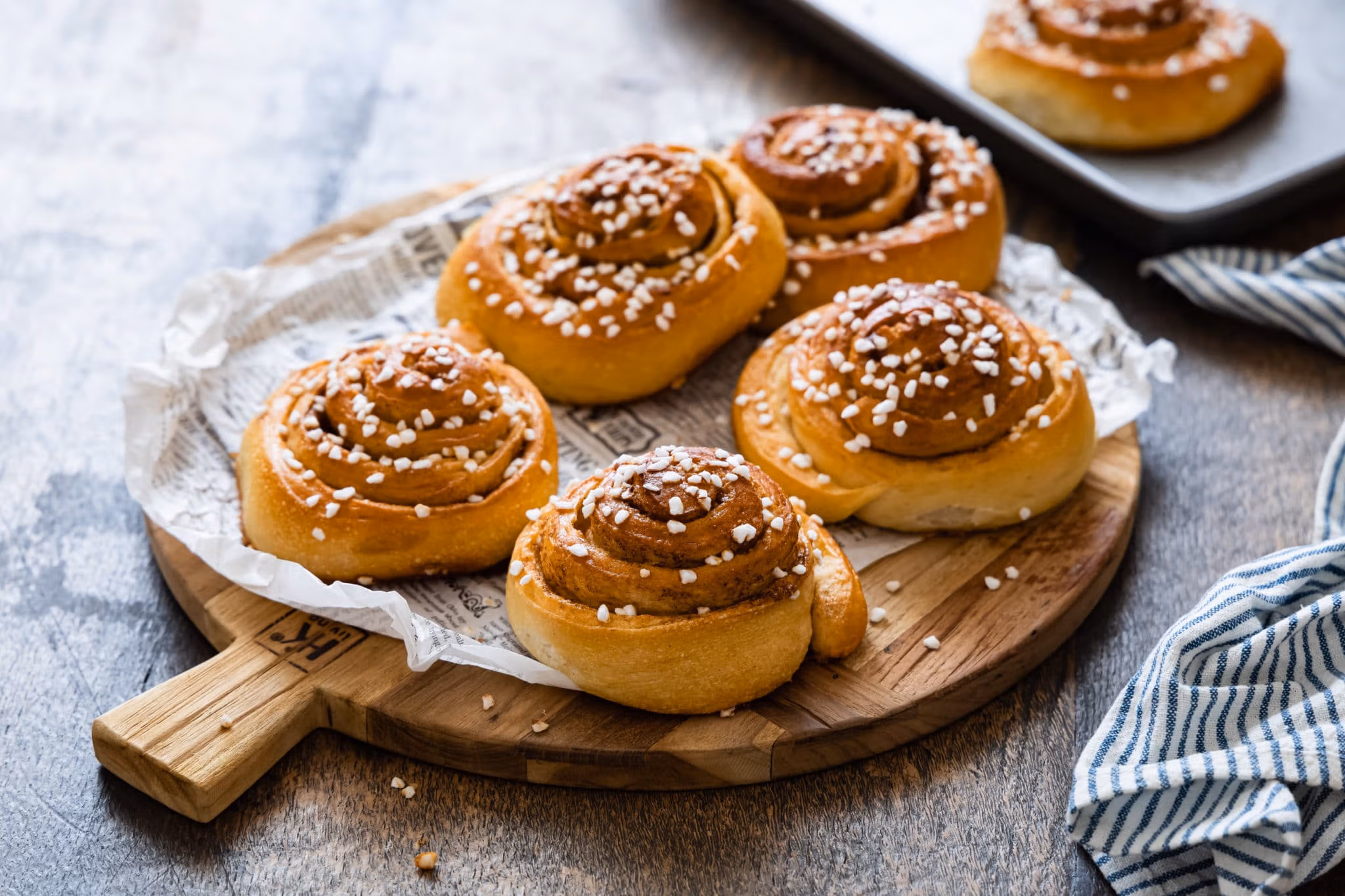 Schwedische Zimtschnecken Kanelbullar mit Hagelzucker bestreut auf einem rustikalen Holzbrett.