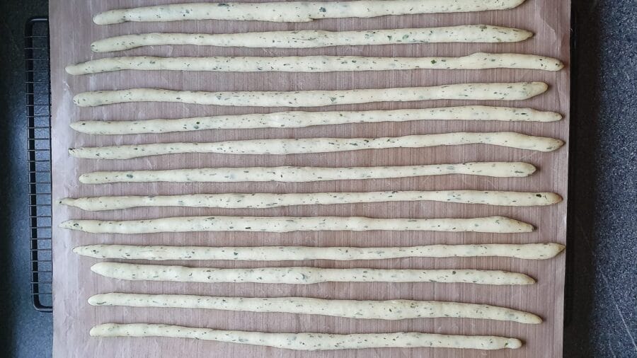 Geformte Grissini auf einem mit Backpapier belegtem Backblech.