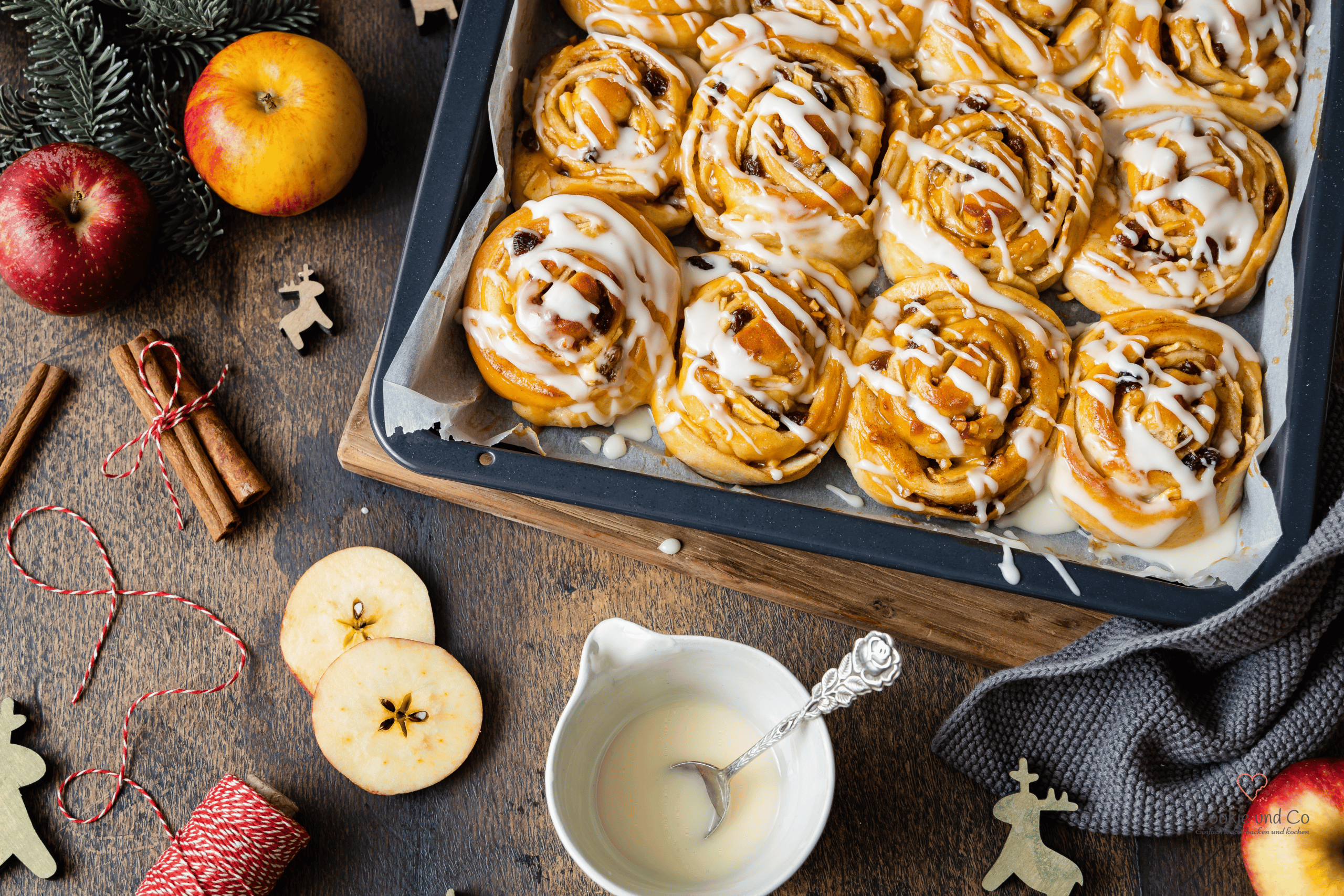Saftige Bratapfel-Zimtschnecken aus Hefeteig auf einem Holztisch mit weihnachtlicher Deko.